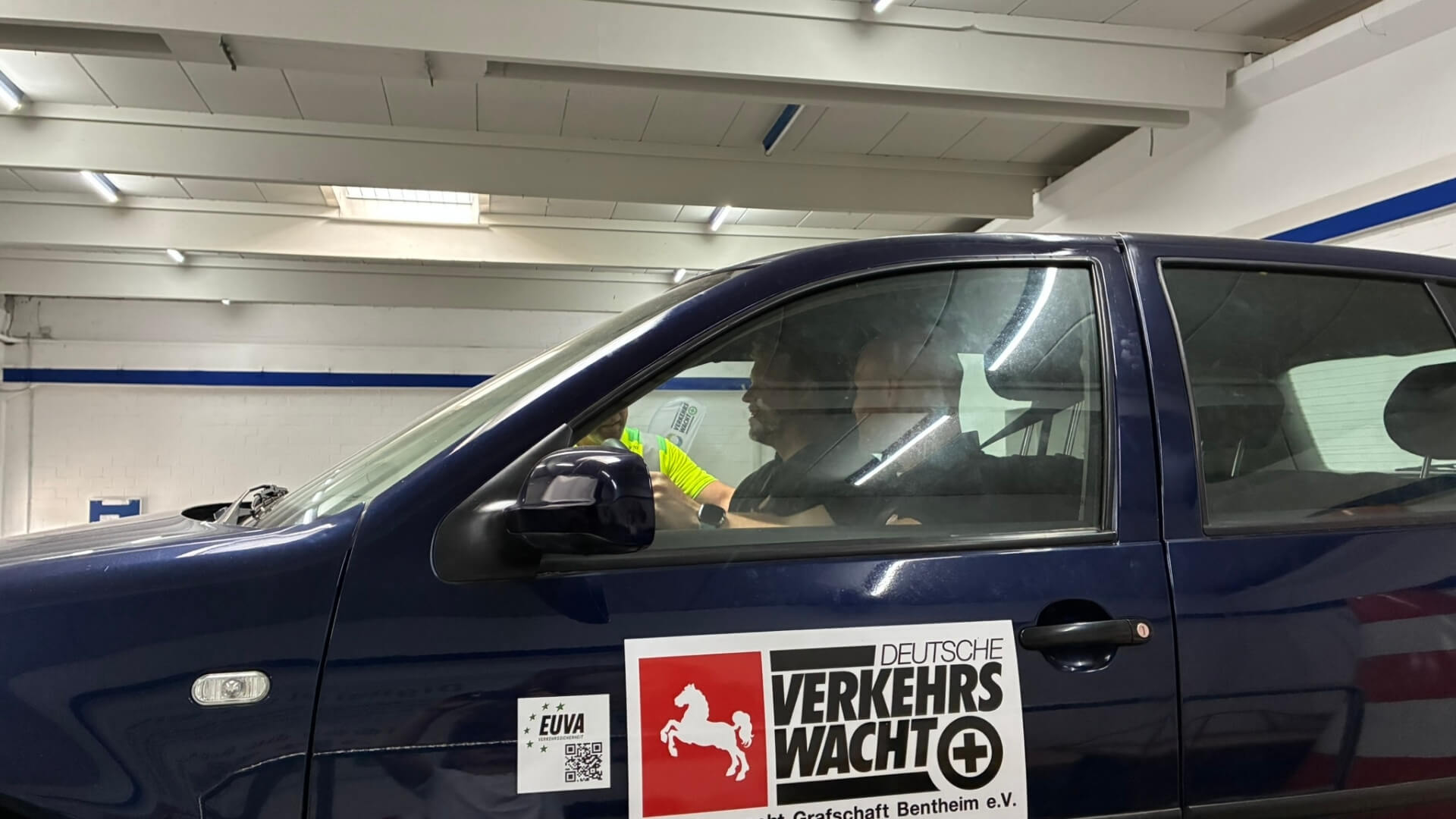 Person sitzt in einem Fahrzeug der Deutschen Verkehrswacht während einer praktischen Fahrsicherheitsübung in einer Halle.